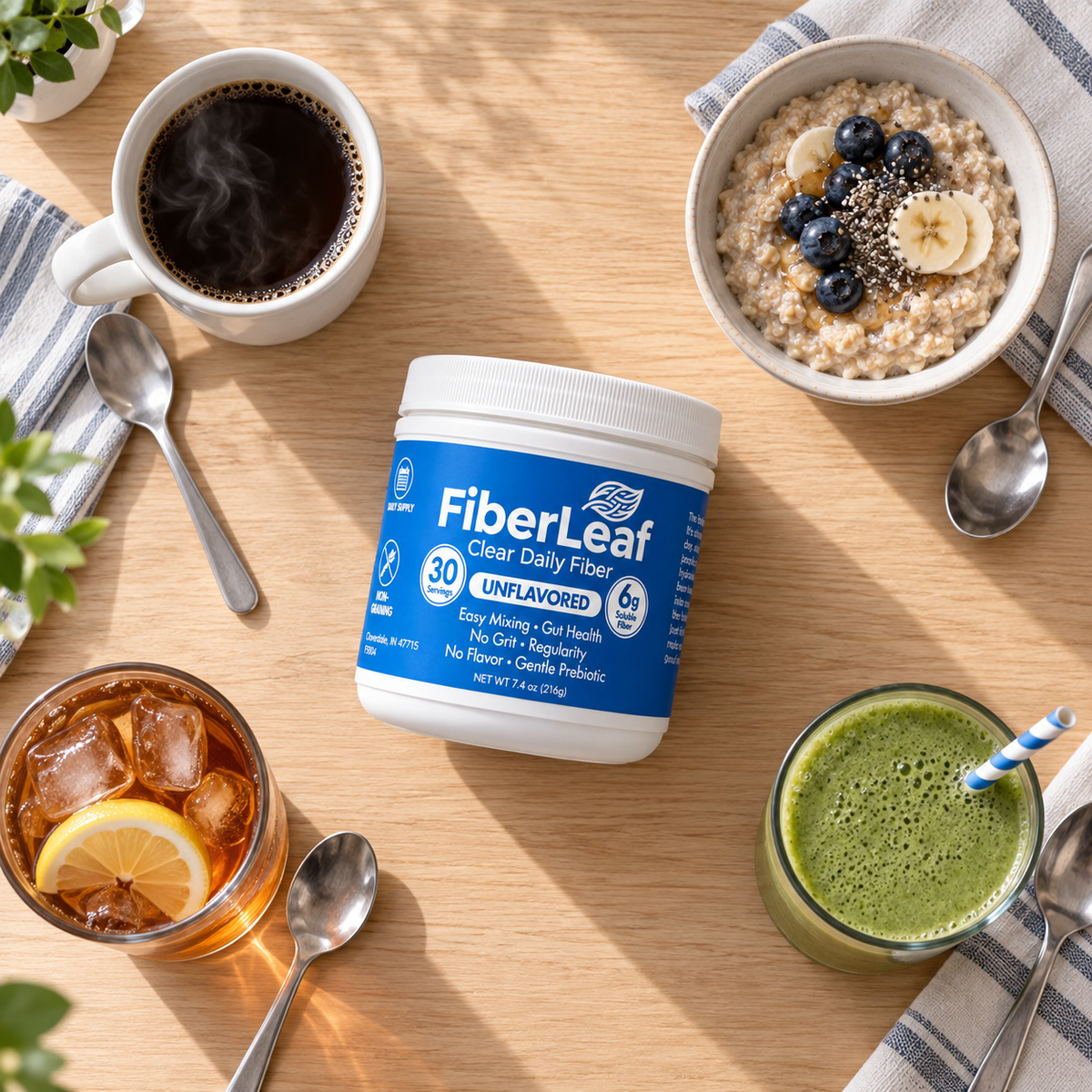 Overhead view of a FiberLeaf can surrounded by a mug of black coffee, a bowl of oatmeal with berries, a glass of iced tea with lemon, and a green smoothie on a wooden table.